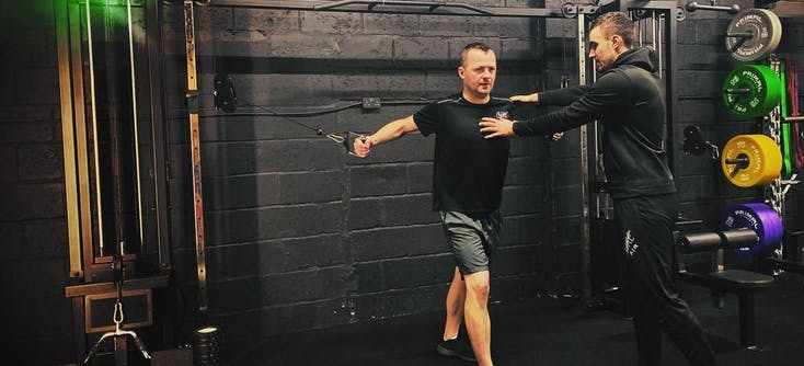 A fitness instructor helping his client with weight training