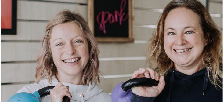 Helen and Maggie, owners of Spark Life, posing with kettlebells in their fitness studio