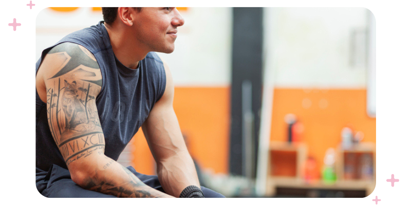 A fit young man sitting at the gym, smiling.