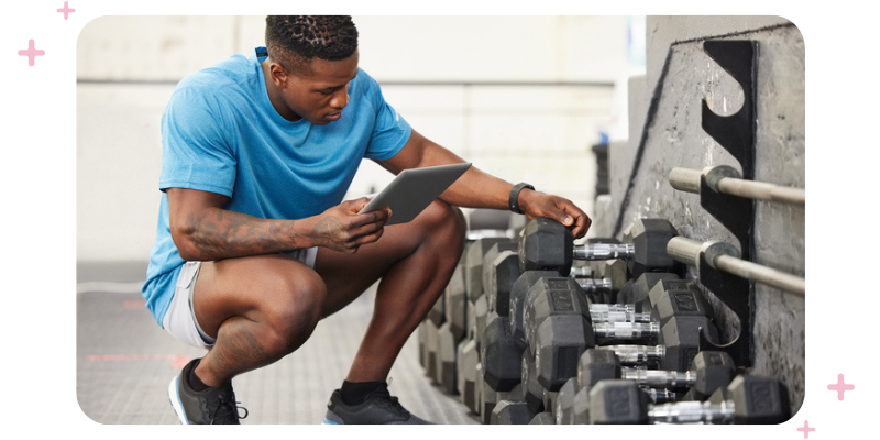 A man in workout gear holding a clipboard while checking out equipment at the gym.