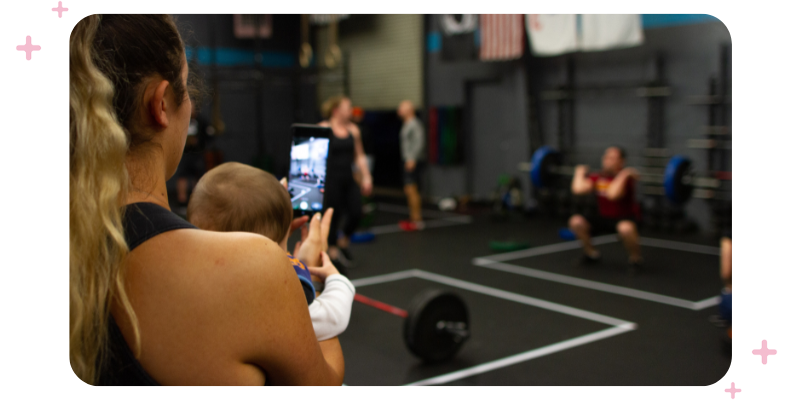 A woman holding a baby and recording an Instagram story at the gym.