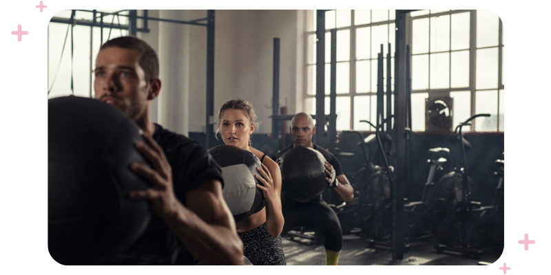 People in the gym holding medicine balls, working out.